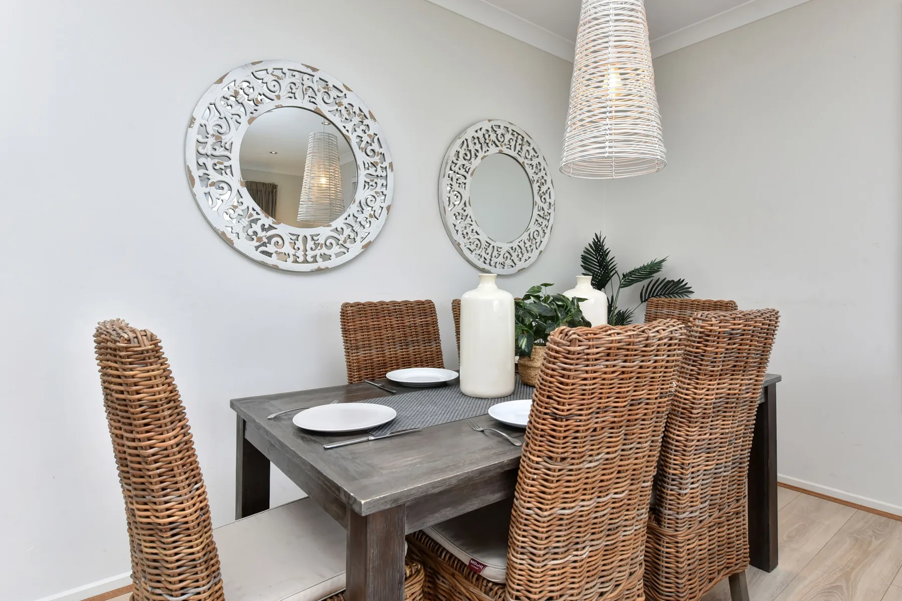 A dining area with a wooden table, woven seating, and decorative wall mirrors.