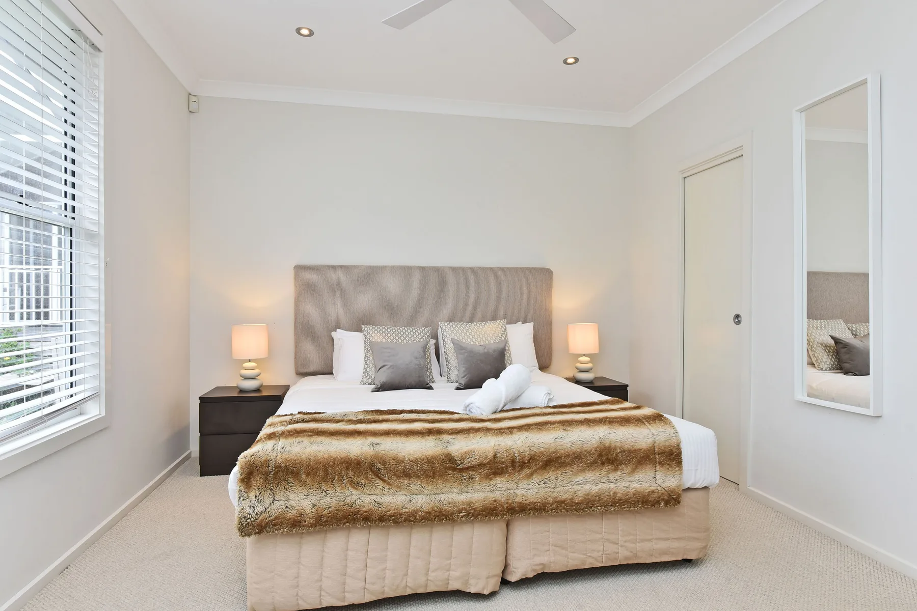 A bedroom with a neatly made bed, bedside tables, and a window.