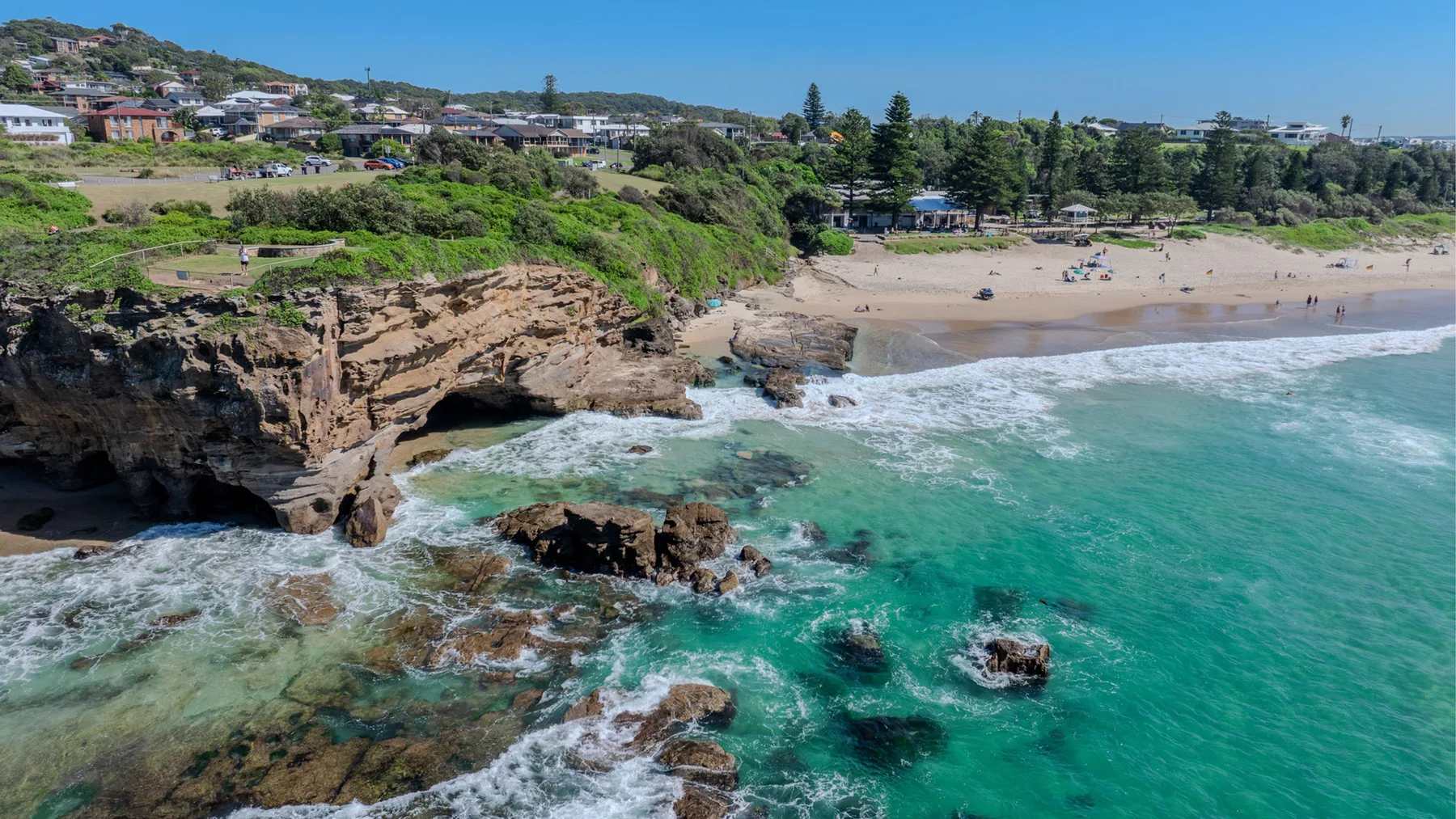 A rocky coastline meets a sandy beach beside clear turquoise water.