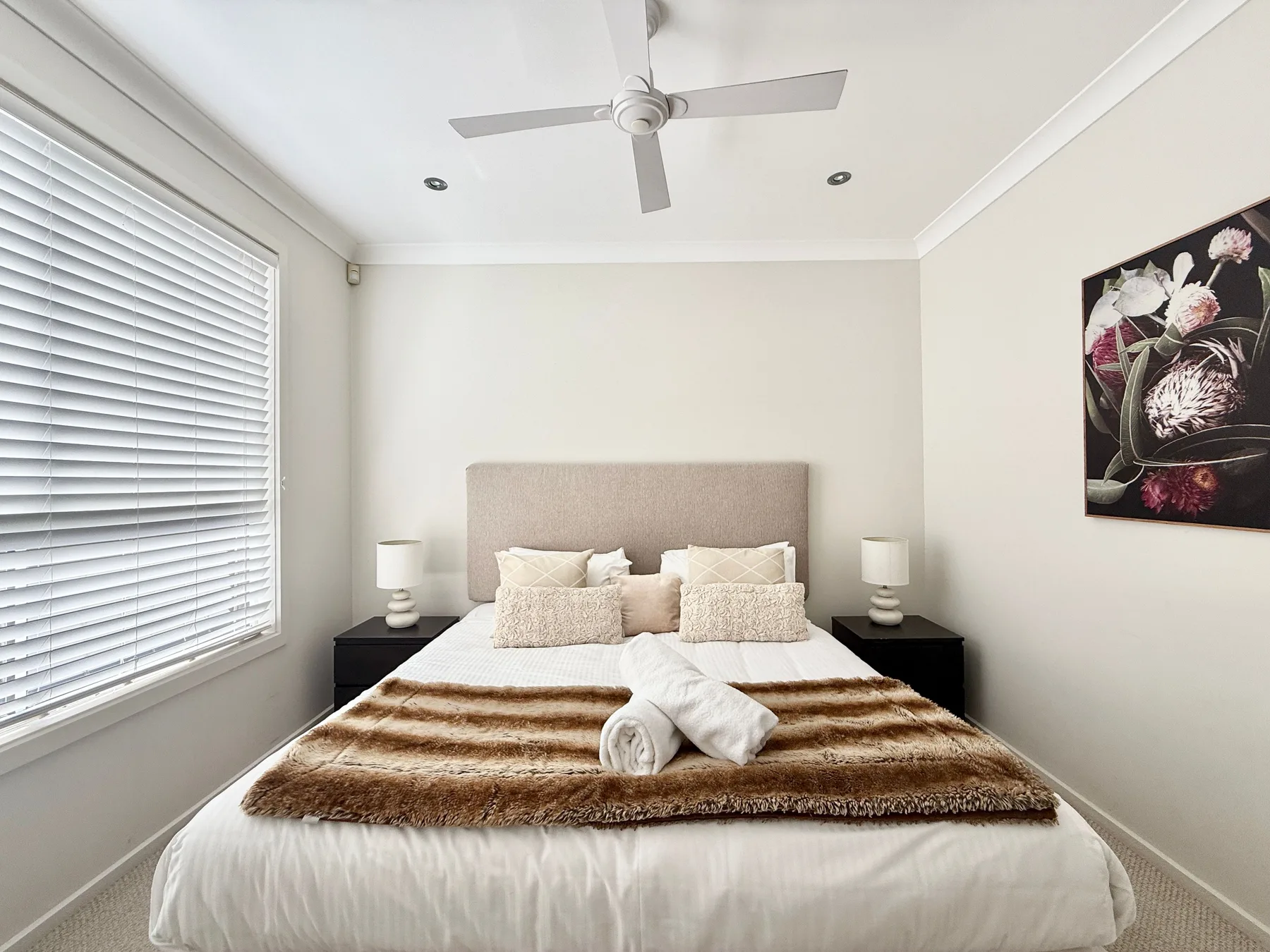 A bright bedroom with a bed, bedside tables, and a large window.