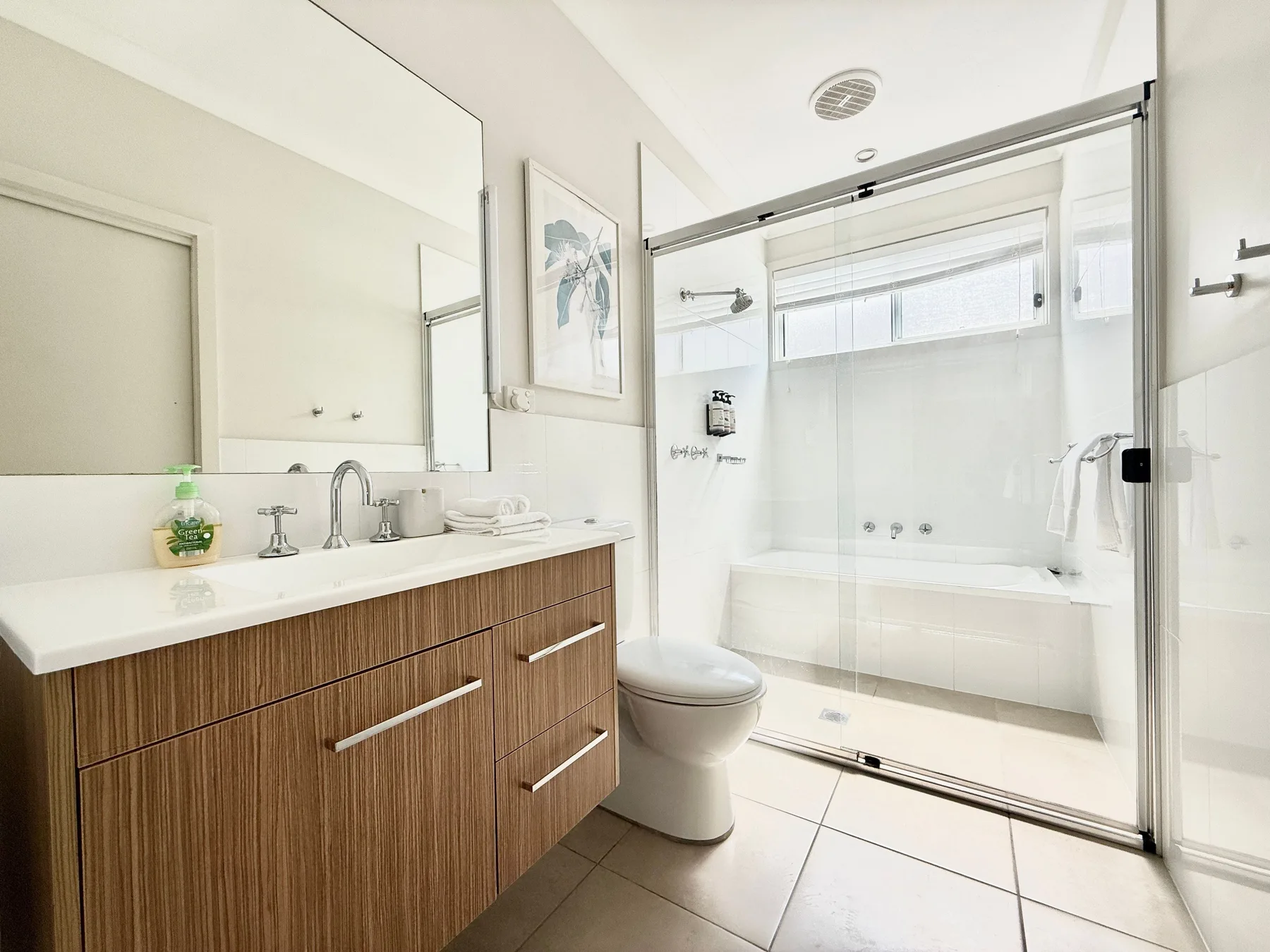 A bright bathroom with a wood-front vanity and a glass-enclosed shower.