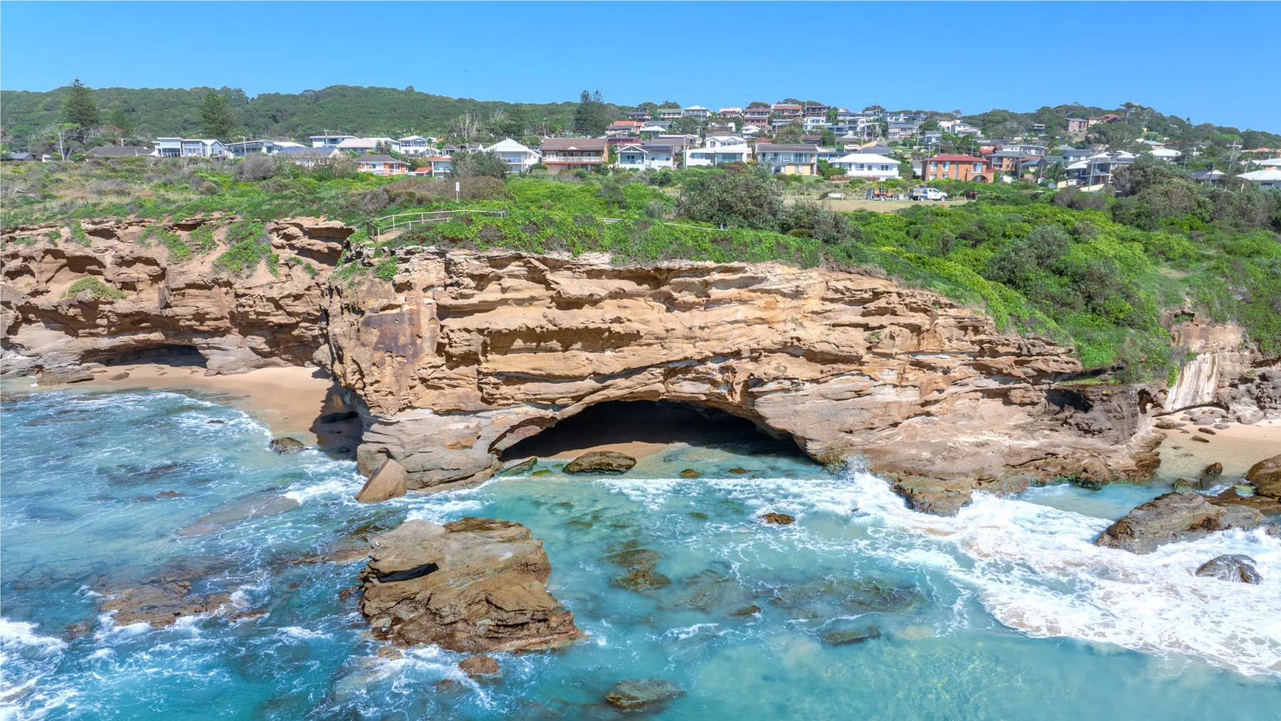 A rocky coastline with waves washing beneath a natural rock arch.