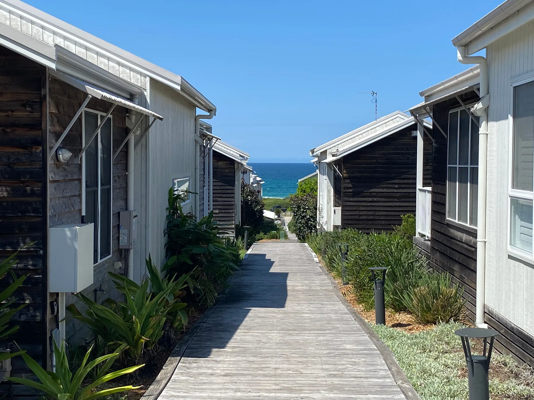 A wooden walkway runs between buildings toward the ocean.