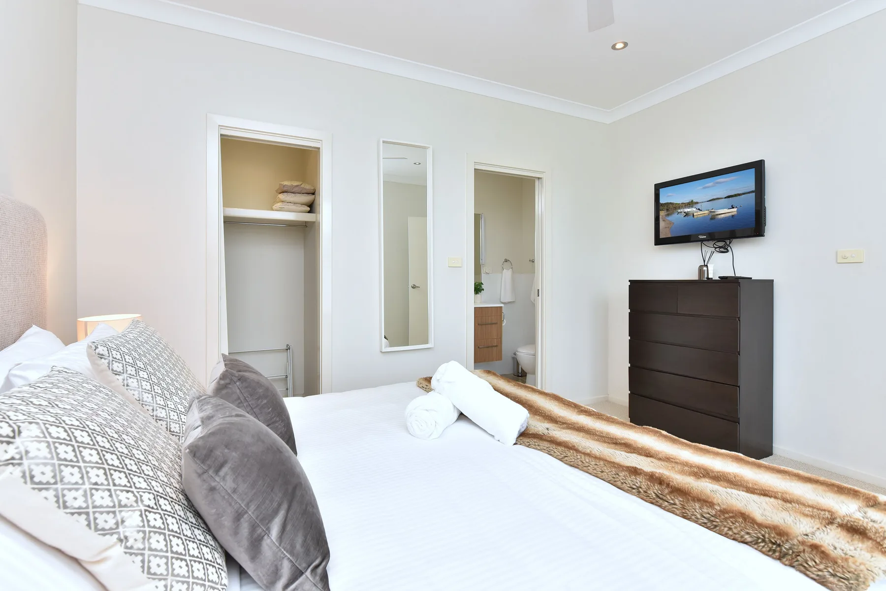A bright bedroom with a neatly made bed and a television above a dresser.
