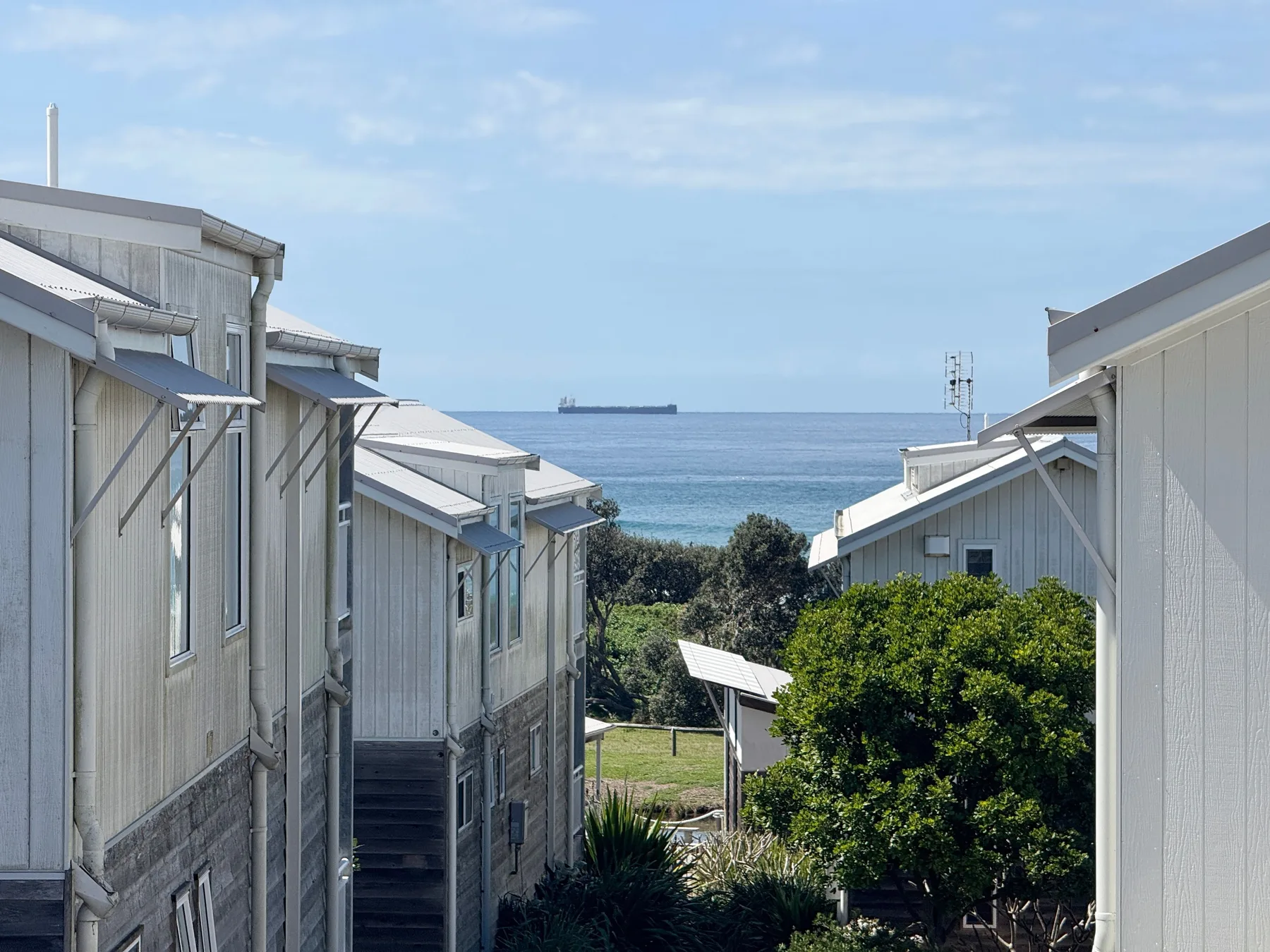 A coastal view between buildings overlooks the ocean and a distant ship.