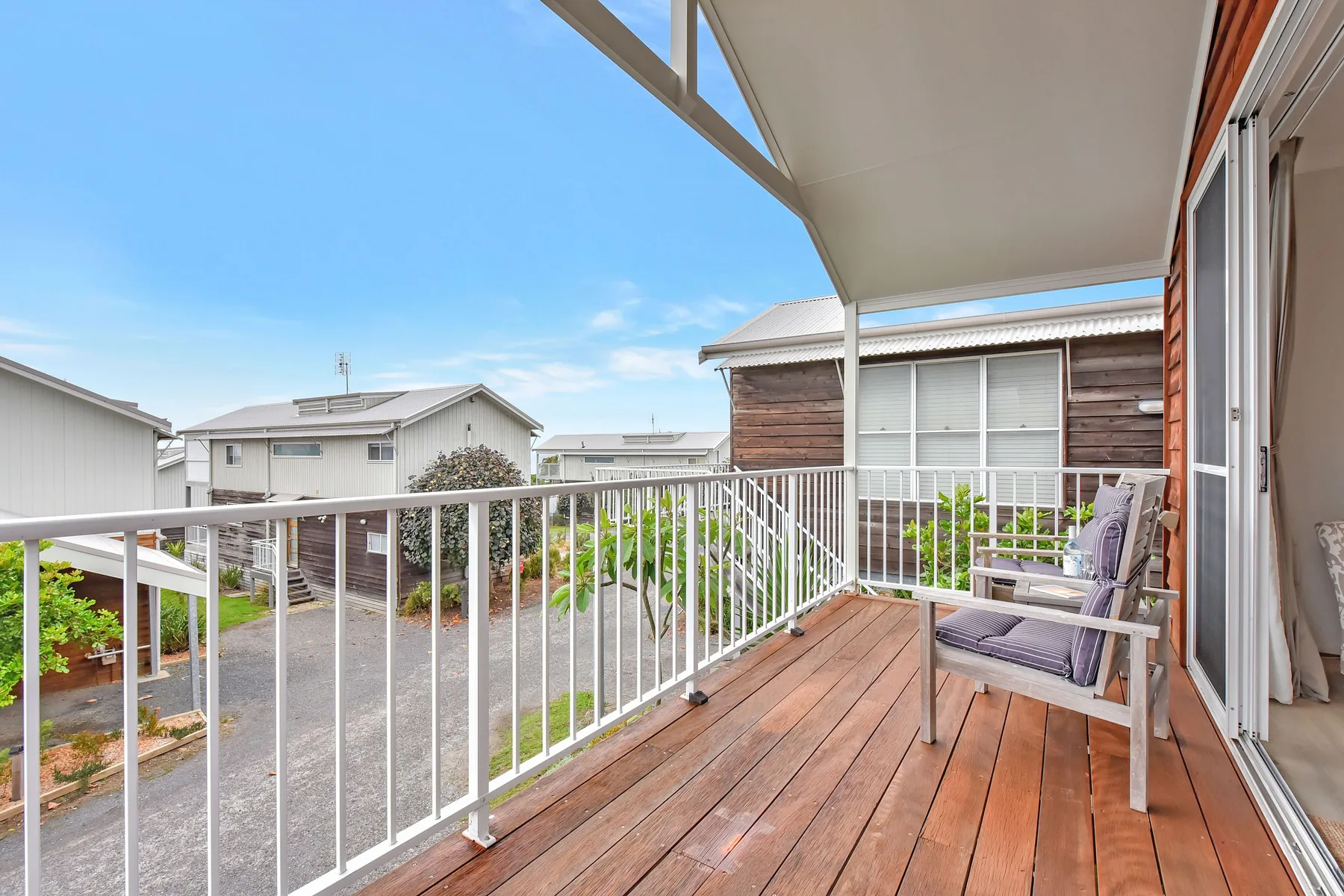 A covered balcony has wooden decking, white railings, and outdoor seating.