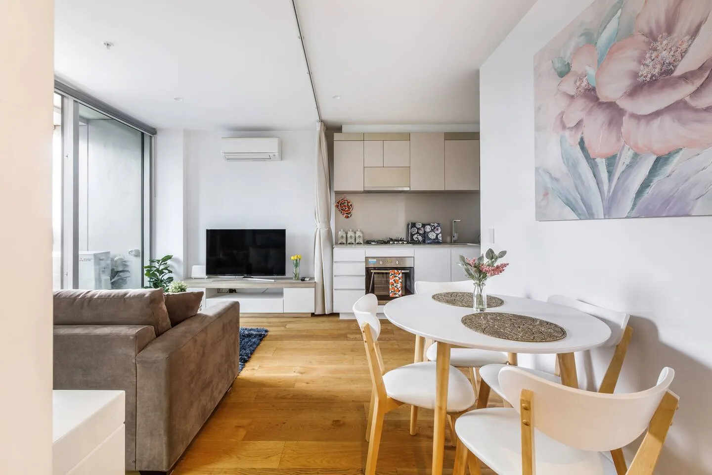 A living and dining area with a television and a table beside large windows.