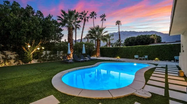 Una piscina iluminada está rodeada de jardines bajo un cielo colorido al atardecer.