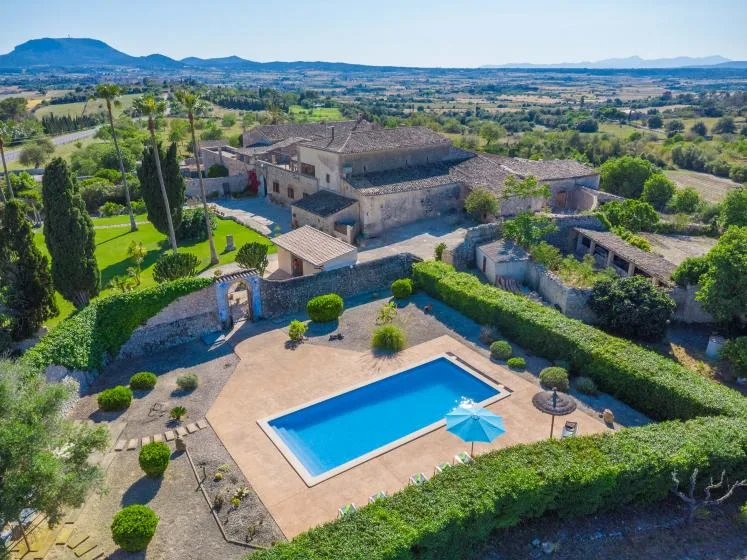 Una vista aérea muestra una piscina junto a una casa rural y jardines.