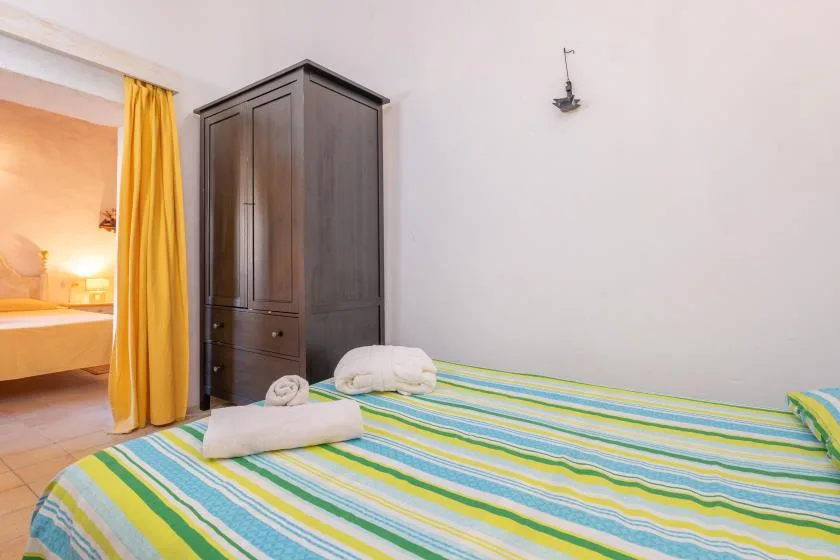 A bedroom with a striped bedspread and a dark wardrobe beside an open doorway.