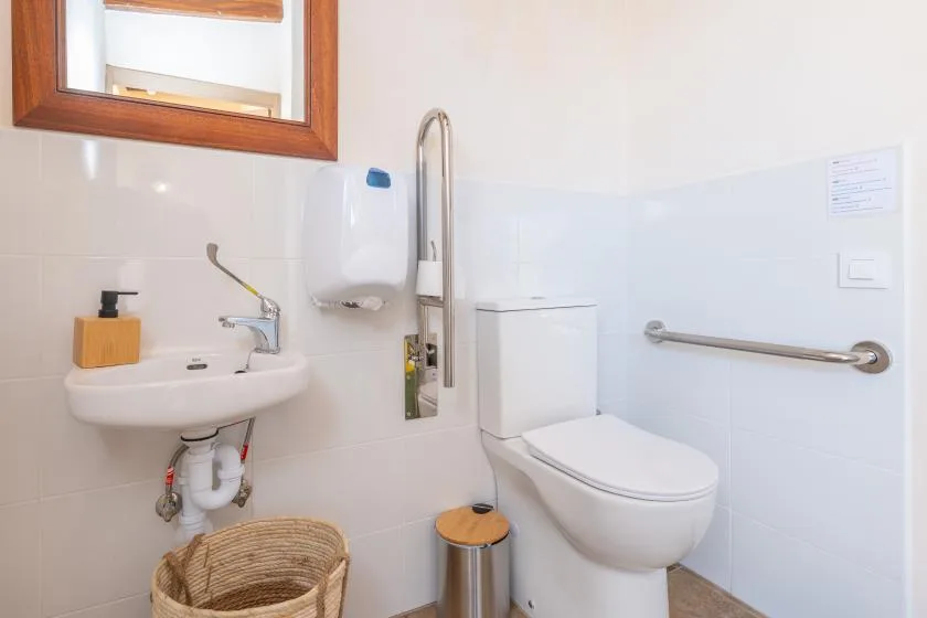 A bright bathroom with a wall-mounted sink and toilet beside a grab bar.