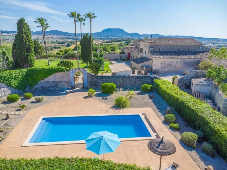 Una piscina está en un patio ajardinado con colinas a lo lejos.