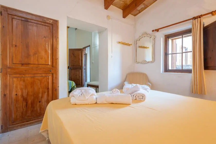A bedroom with a bed, folded towels, and a window beside the door.