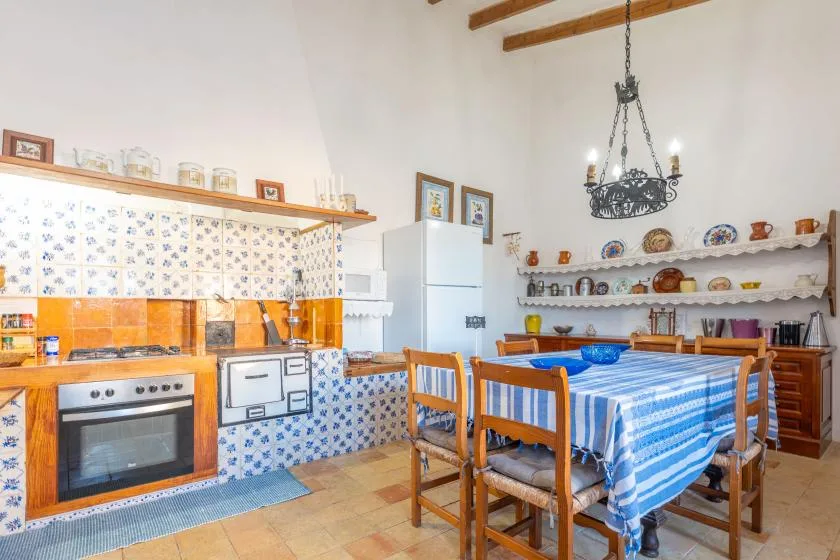 A rustic kitchen and dining area with a blue-striped tablecloth and exposed ceiling beams.