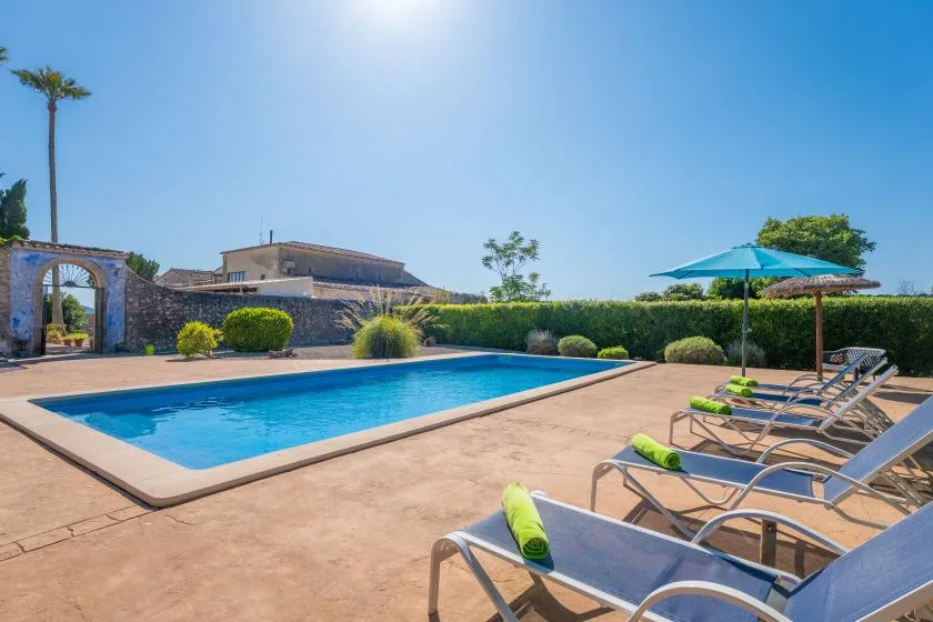 An outdoor swimming pool is surrounded by lounge seating and a shade umbrella.