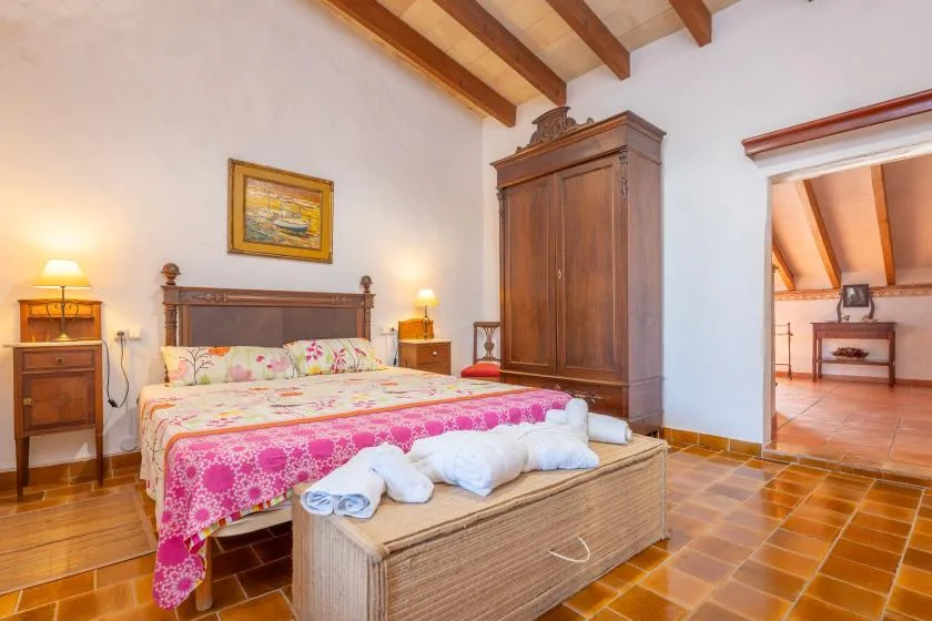 A bedroom with a floral bedspread, wooden wardrobe, and exposed ceiling beams.