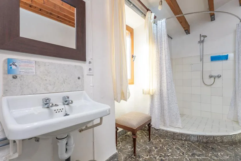 A bright bathroom with a sink, shower, and small upholstered stool.