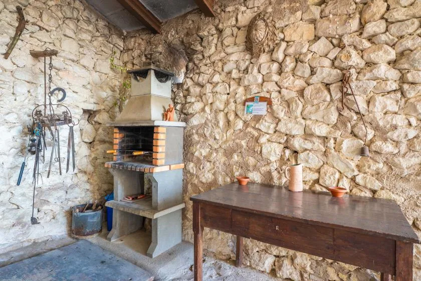 A rustic stone-walled cooking area with a built-in grill and wooden table.