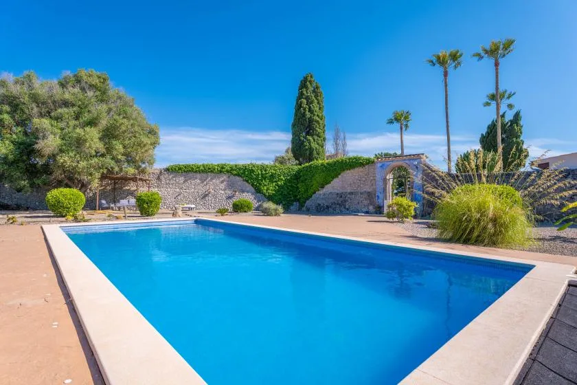 An outdoor swimming pool sits beside a stone wall and landscaped greenery.