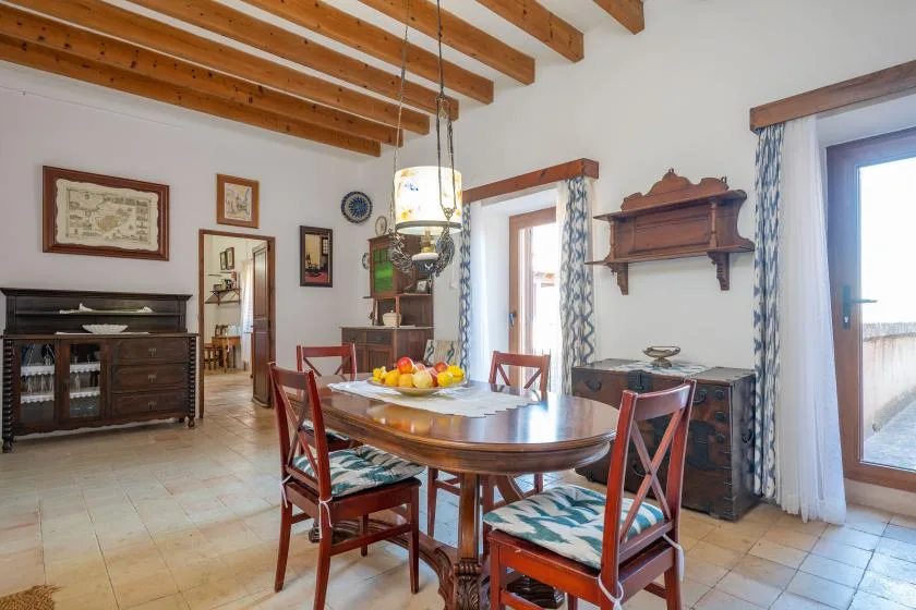 A dining room with a wooden table and chairs beneath exposed ceiling beams.