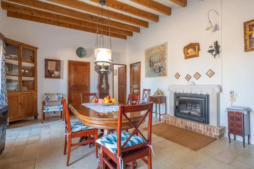 A dining room with a wooden table and a fireplace beneath exposed ceiling beams.