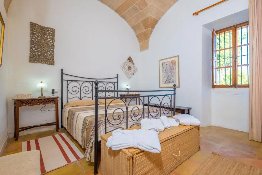 A bedroom with an iron bed, woven chest, and colorful window.