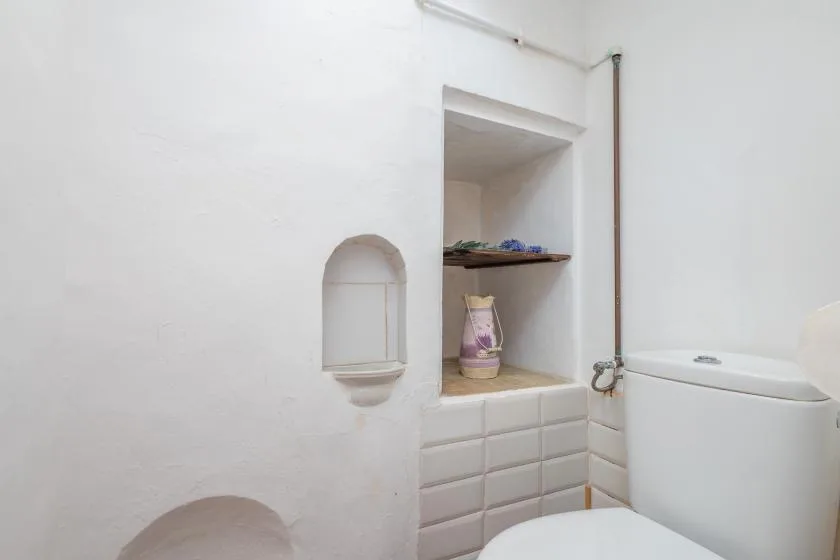 A small bathroom with a toilet, tiled wall, and recessed storage niches.