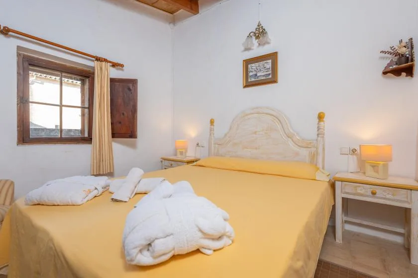 A bedroom with a large bed dressed in yellow and a window with curtains.