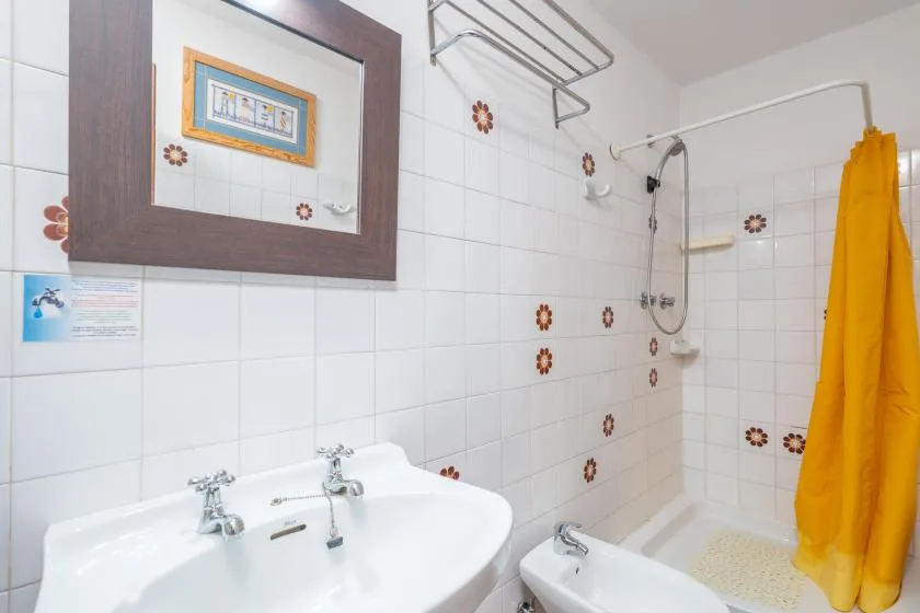 A tiled bathroom with a sink, shower, and bright yellow curtain.