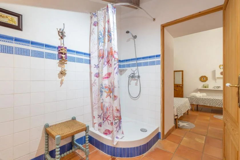 A tiled bathroom with a shower curtain and an open doorway to a bedroom.