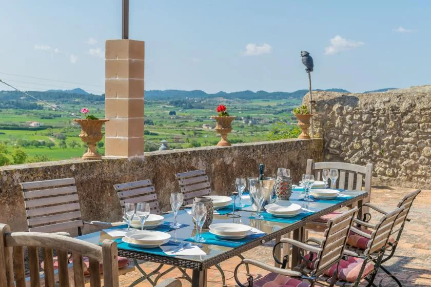 An outdoor dining terrace with a set table overlooking a green valley.
