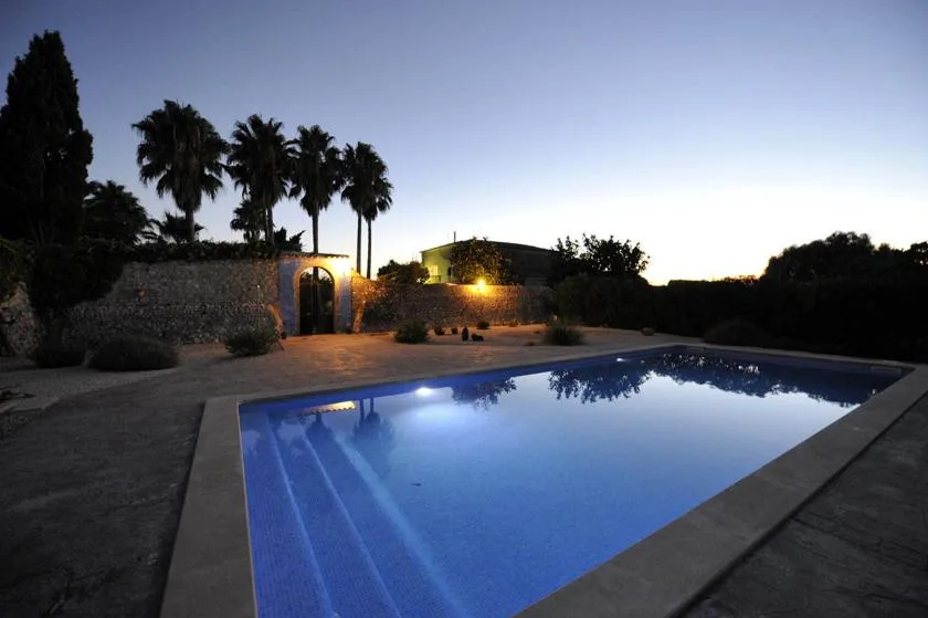 An outdoor swimming pool sits beside a stone wall at dusk.
