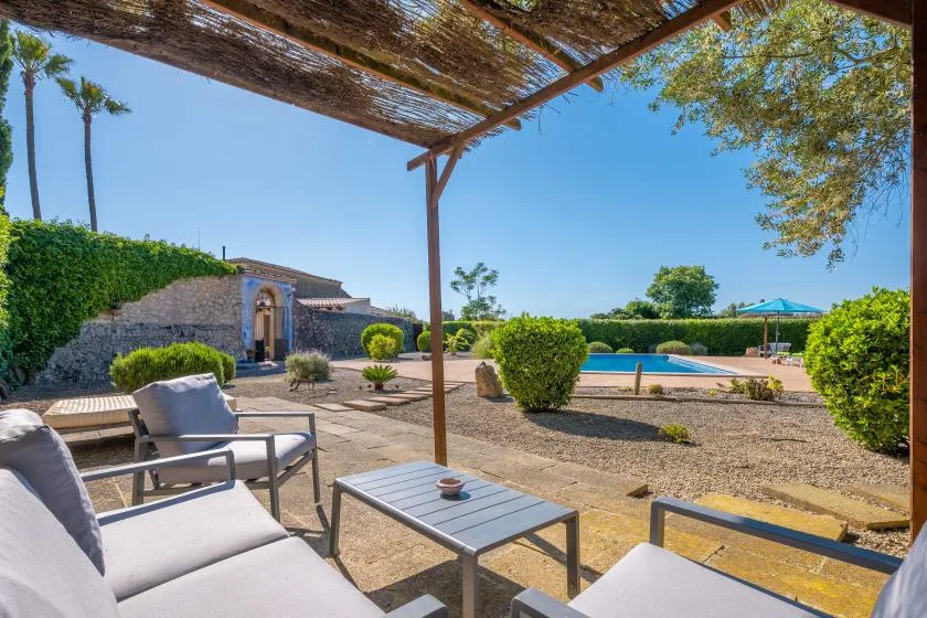 A shaded outdoor patio with seating overlooks a swimming pool and landscaped grounds.