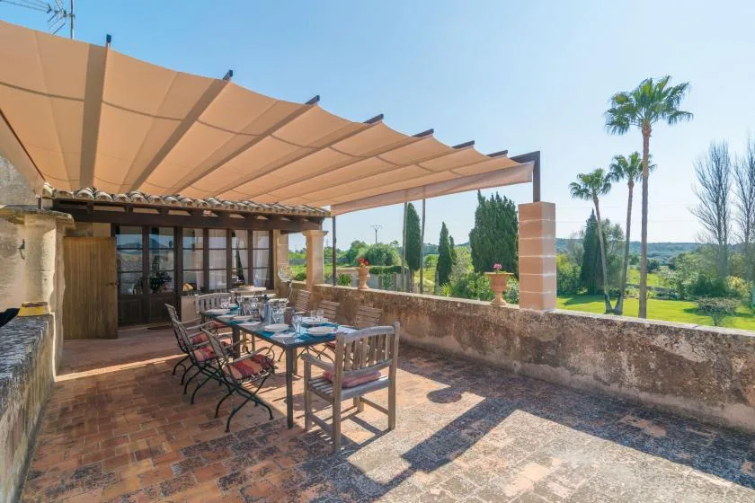 An outdoor dining terrace beneath a fabric canopy, overlooking a green garden.