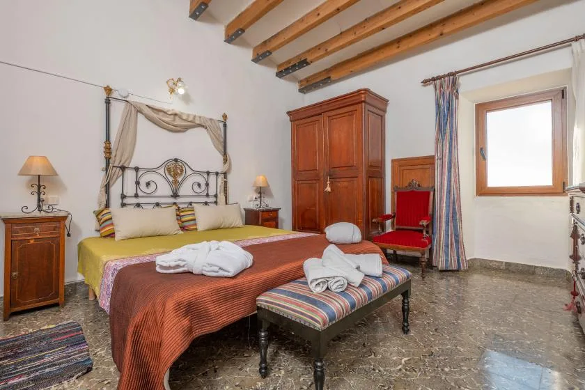 A bedroom with a bed and a striped bench beneath exposed ceiling beams.