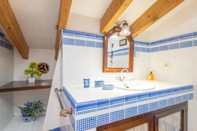 A tiled bathroom vanity with a sink, mirror, and exposed wooden ceiling beams.