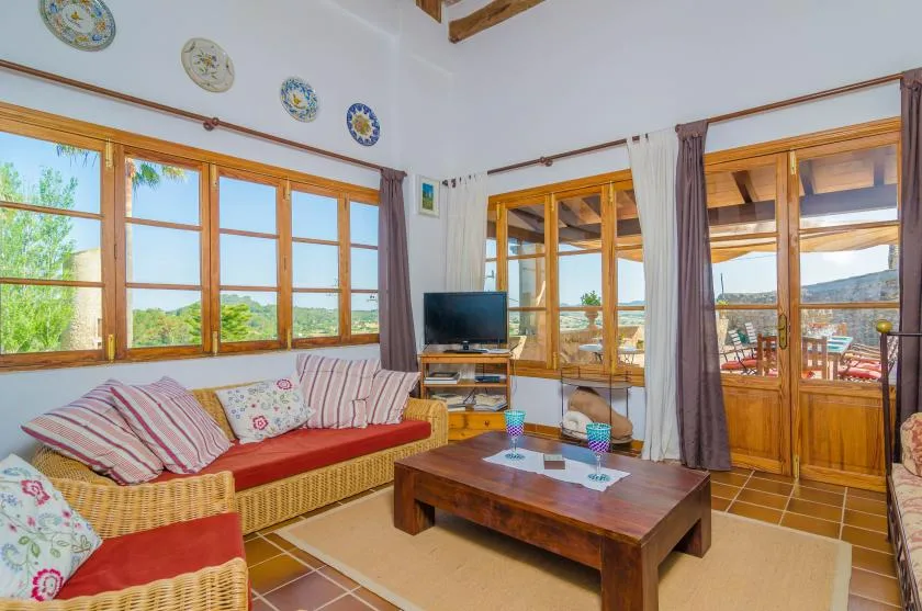 A bright living room has a seating area, wooden coffee table, and large windows.