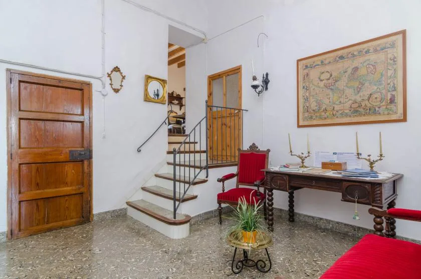 A stairway and wooden door share a room with a table and red seating.