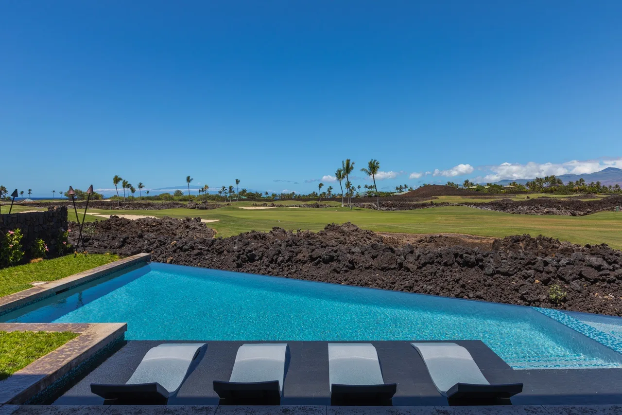 A swimming pool overlooks a grassy landscape with palm trees and distant hills.