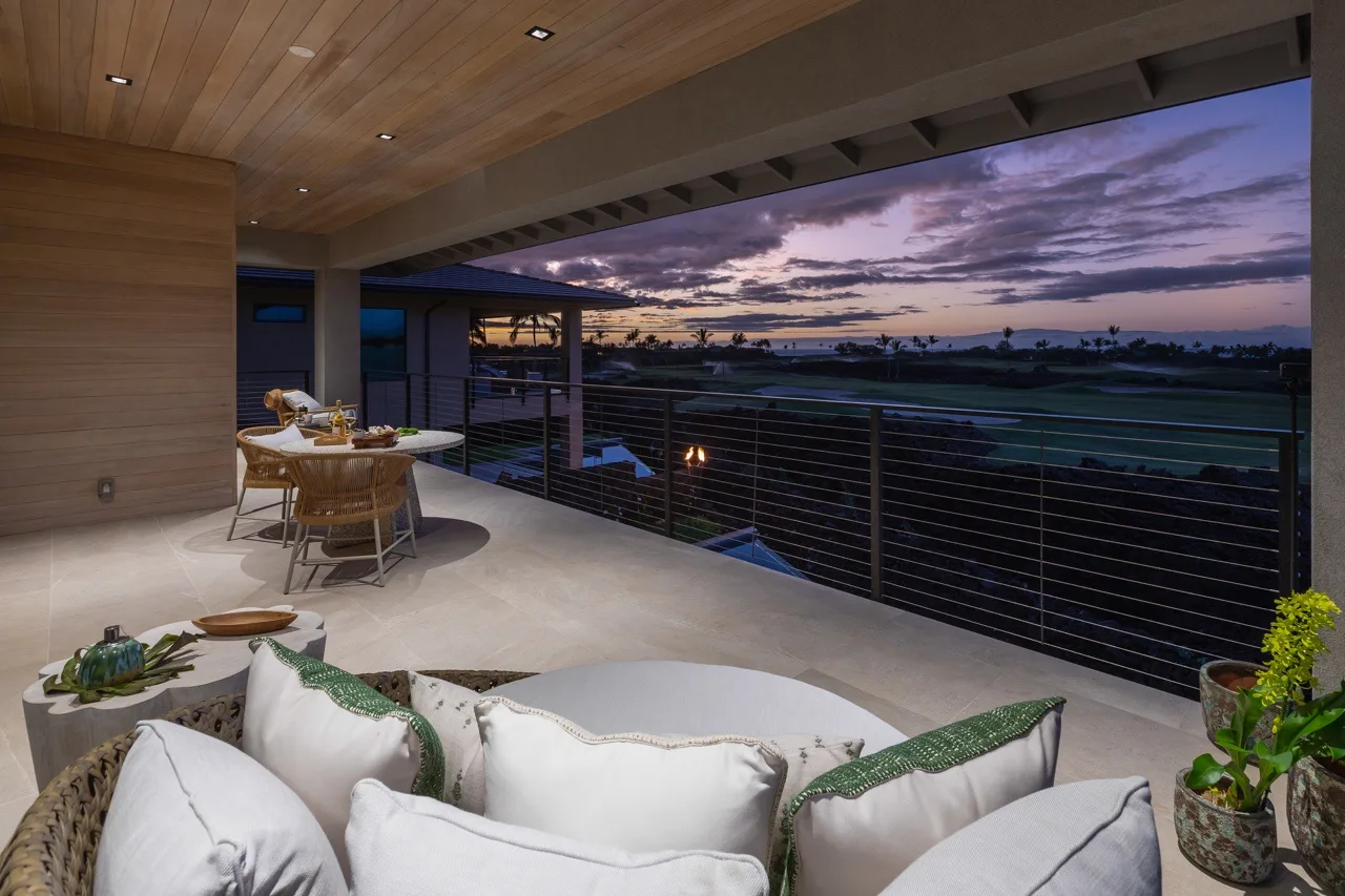 A covered outdoor terrace with seating overlooks a landscape at sunset.