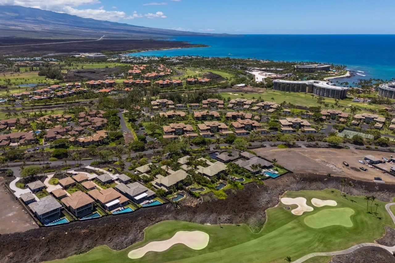 An aerial view of a coastal neighborhood beside a golf course and blue ocean.