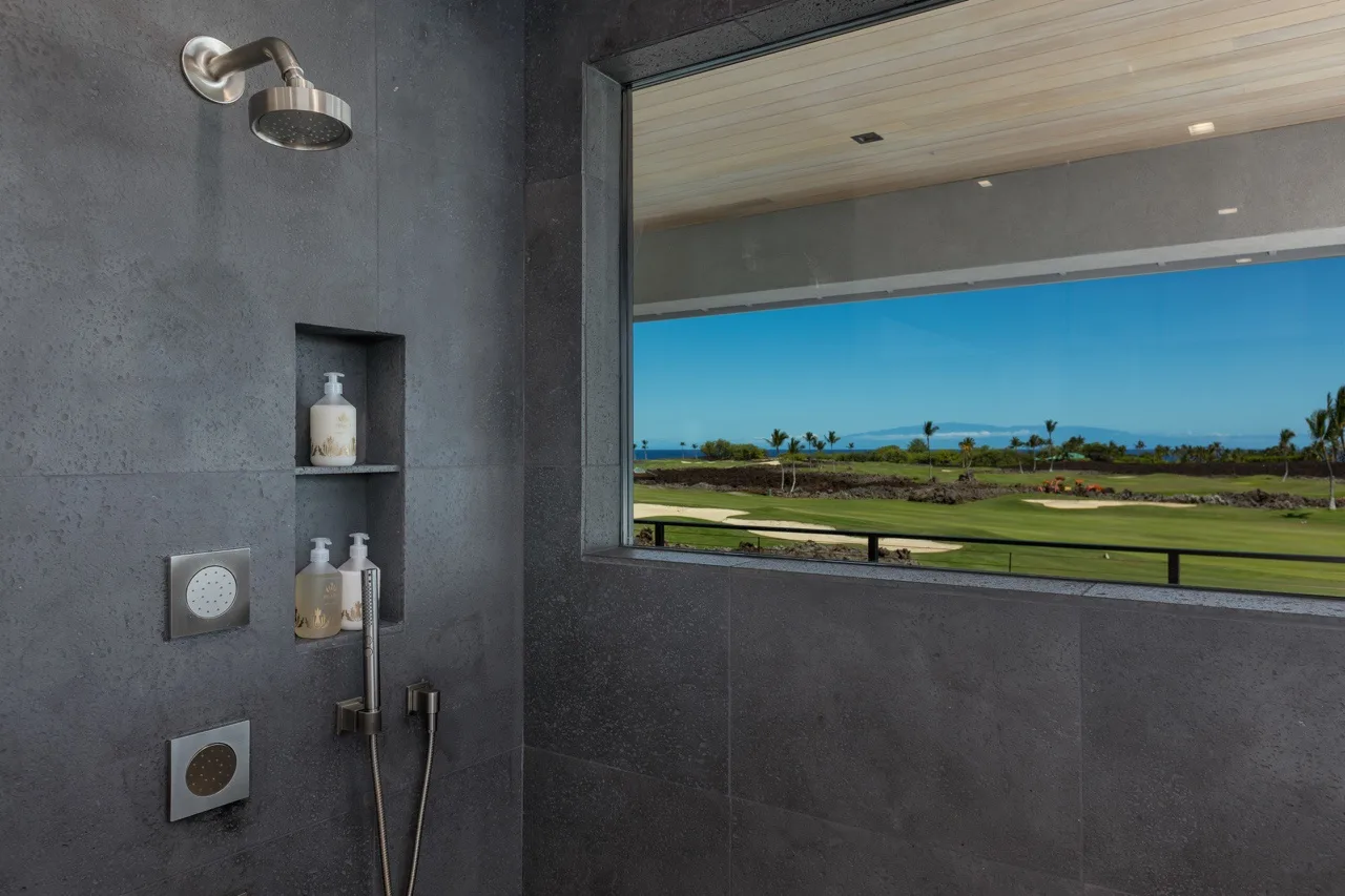 A modern shower area overlooks green grounds and a blue ocean horizon through a wide window.