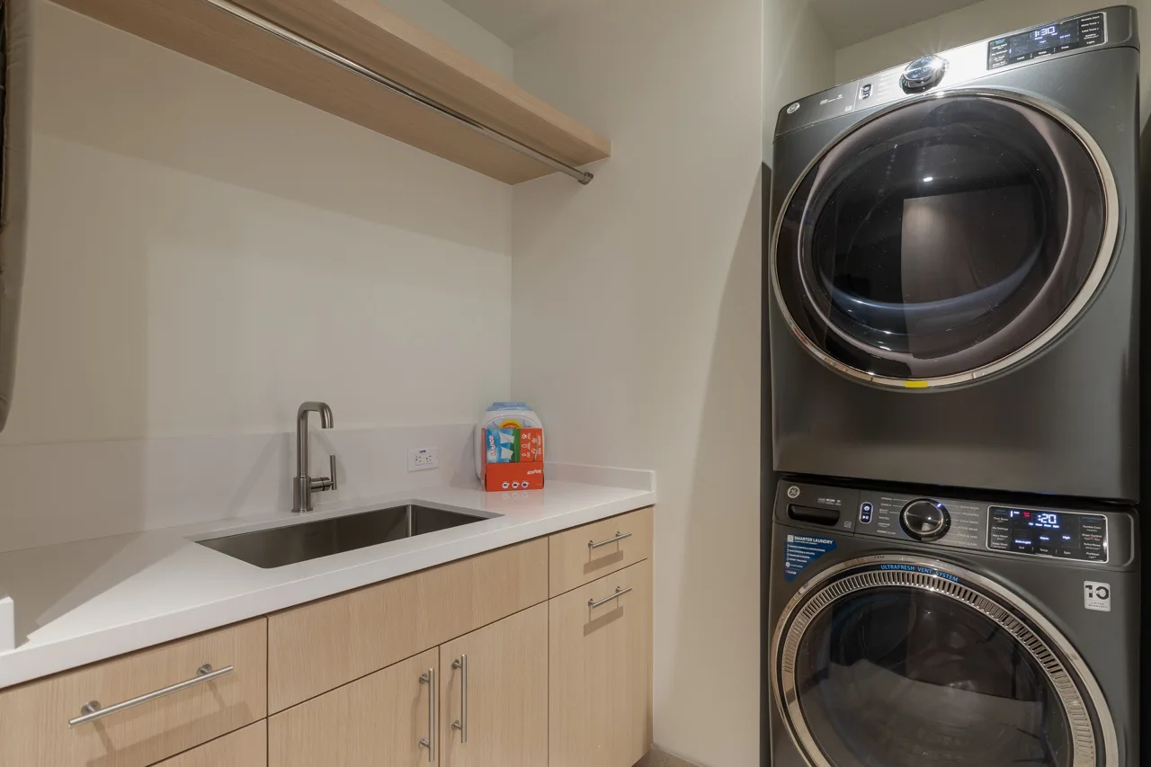A laundry room with a stacked washer and dryer beside a sink and counter.