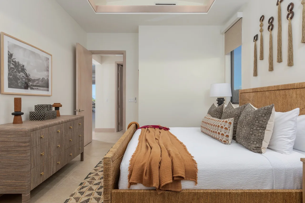 A bedroom with a bed, patterned cushions, and a wooden dresser.
