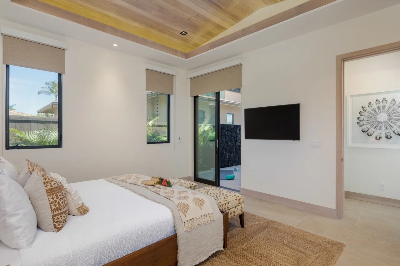 A bedroom with a bed, windows, and a wall-mounted television.
