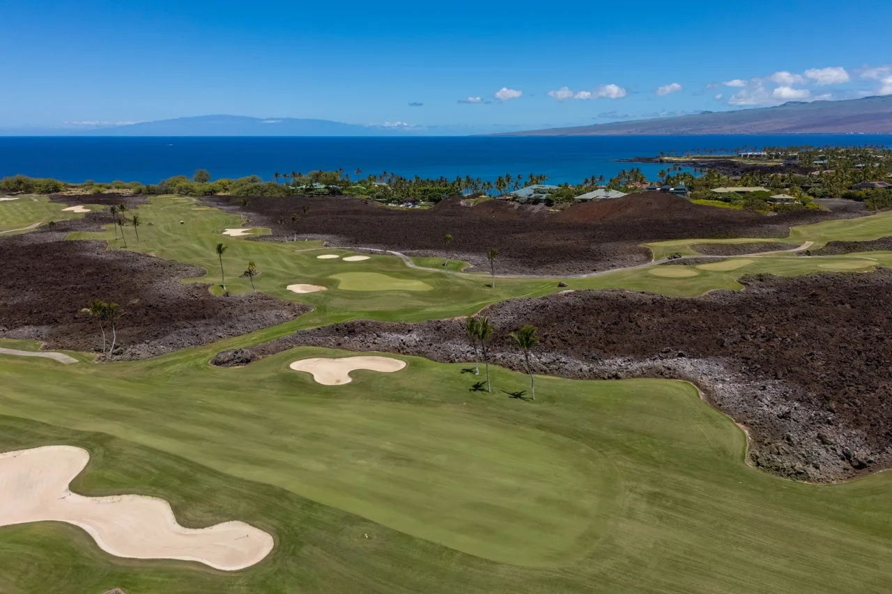 A golf course with green fairways and sand bunkers overlooking the ocean.