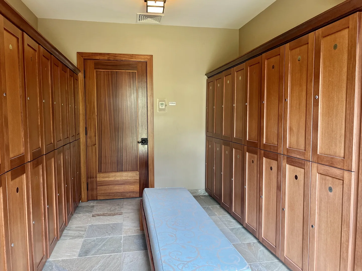 A locker room with rows of wooden lockers and a padded bench.