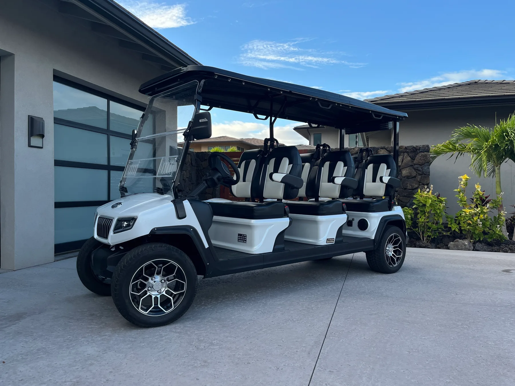A white open-sided golf cart is parked on a paved driveway beside a modern building.