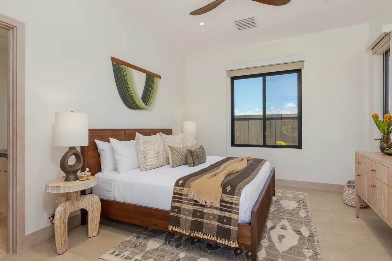 A bedroom with a neatly made bed, patterned blanket, and window.