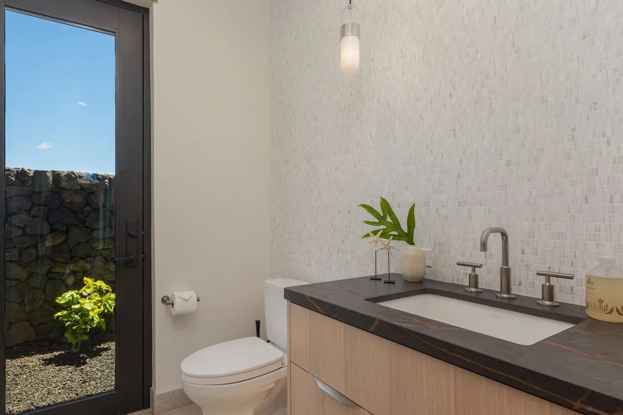 A bright bathroom with a vanity, sink, and toilet beside a glass door.